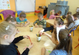 Sześcioro dzieci siedzi przy stoliku i koloruje sylwetę dziecka.